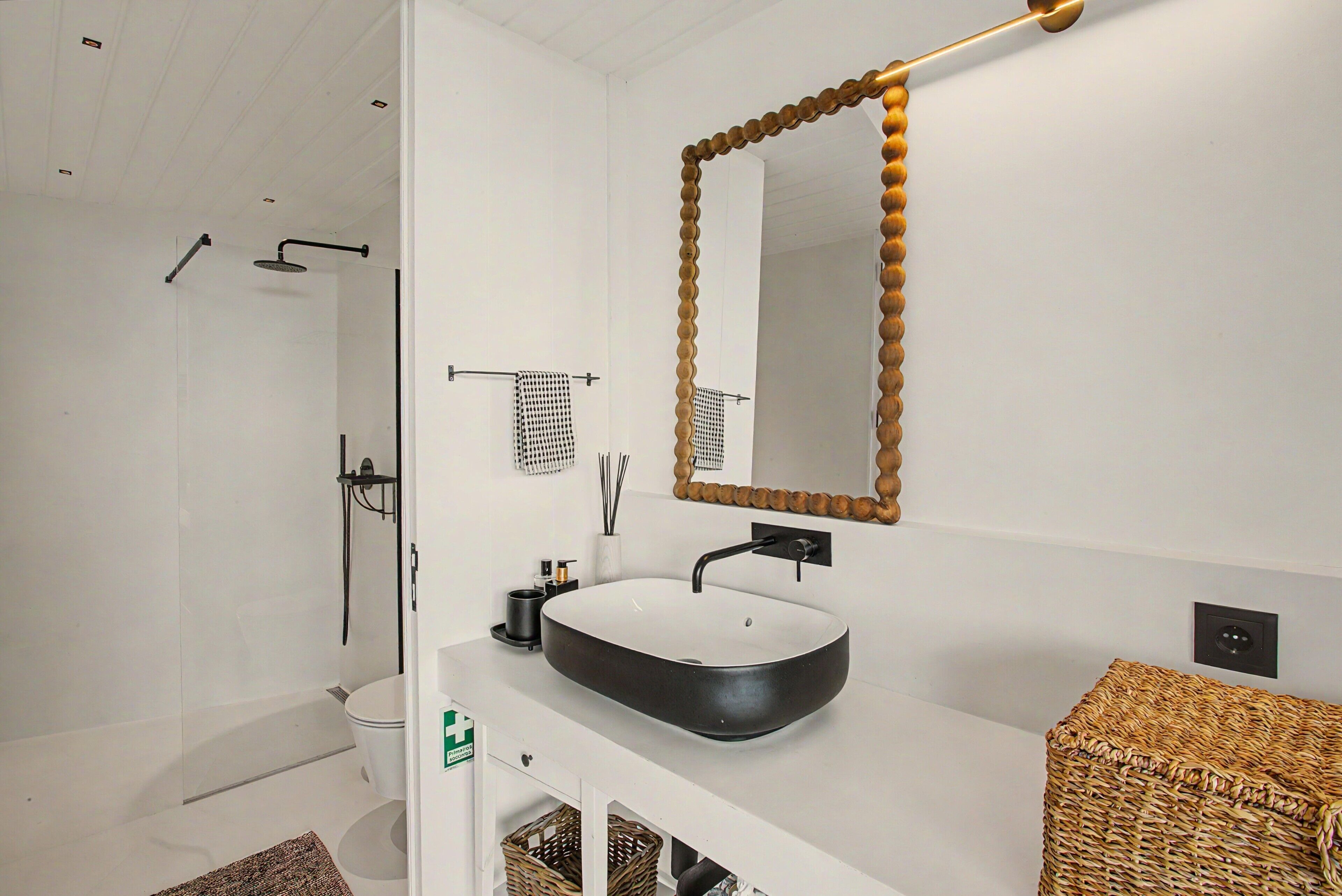 A modern bathroom with a large oval sink, a mirror with a wooden frame, a shower, and a white vanity.