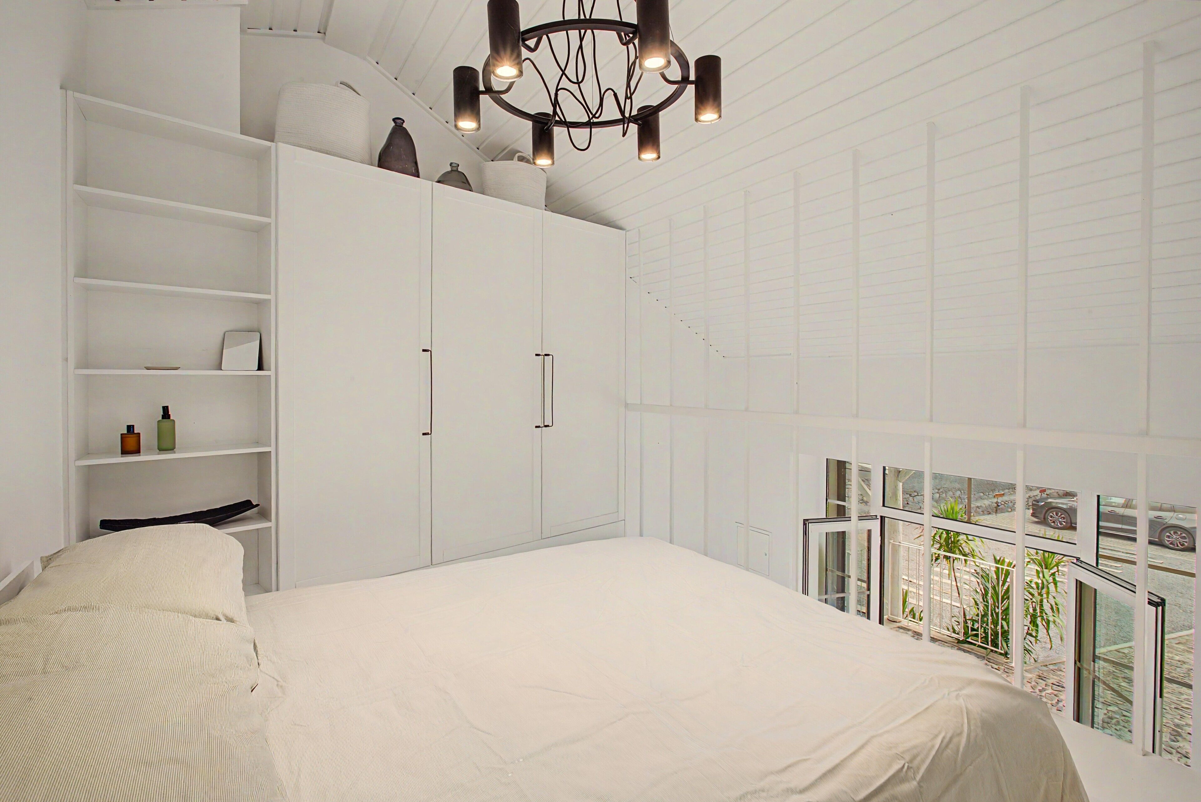 A bedroom with a large bed, built-in wardrobe, and a view through a balcony.