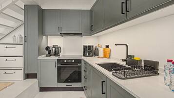 A modern kitchen with grey cabinets, a built-in oven, a sink with a faucet, and a coffee maker.