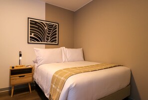 A neatly made bed with a white and beige bedspread, a small wooden nightstand with a lamp, and a wall-mounted abstract art piece. - w Cozy Loft in the Heart of Barranco (Lima)