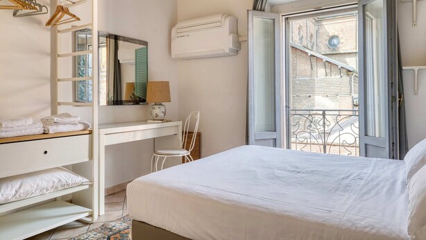 Ein Schlafzimmer mit Bett, Schreibtisch, Stuhl, Kleiderschrank und Fenster mit Blick auf ein Gebäude.