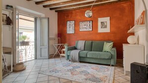 Ein Wohnzimmer mit einem grünen Sofa, einem gemusterten Teppich, einer weißen Kommode und einer Decke mit freiliegenden Balken.