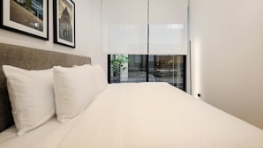 Moderni hotellihuone, jossa on suuri sänky, kaksi kehystettyä taulua seinällä ja lasiovesta avautuva näkymä kaupunkiin.
