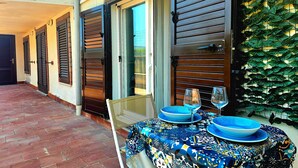 Eine Terrasse mit Tisch für zwei Personen, eine Tür mit Fensterläden und eine Wand mit einem Blättermotiv.