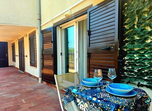 Eine Terrasse mit Tisch für zwei Personen, eine Tür mit Fensterläden und eine Wand mit einem Blättermotiv.