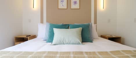 A bed with a checkered pillow, a beige blanket, and two wall-mounted light fixtures.
