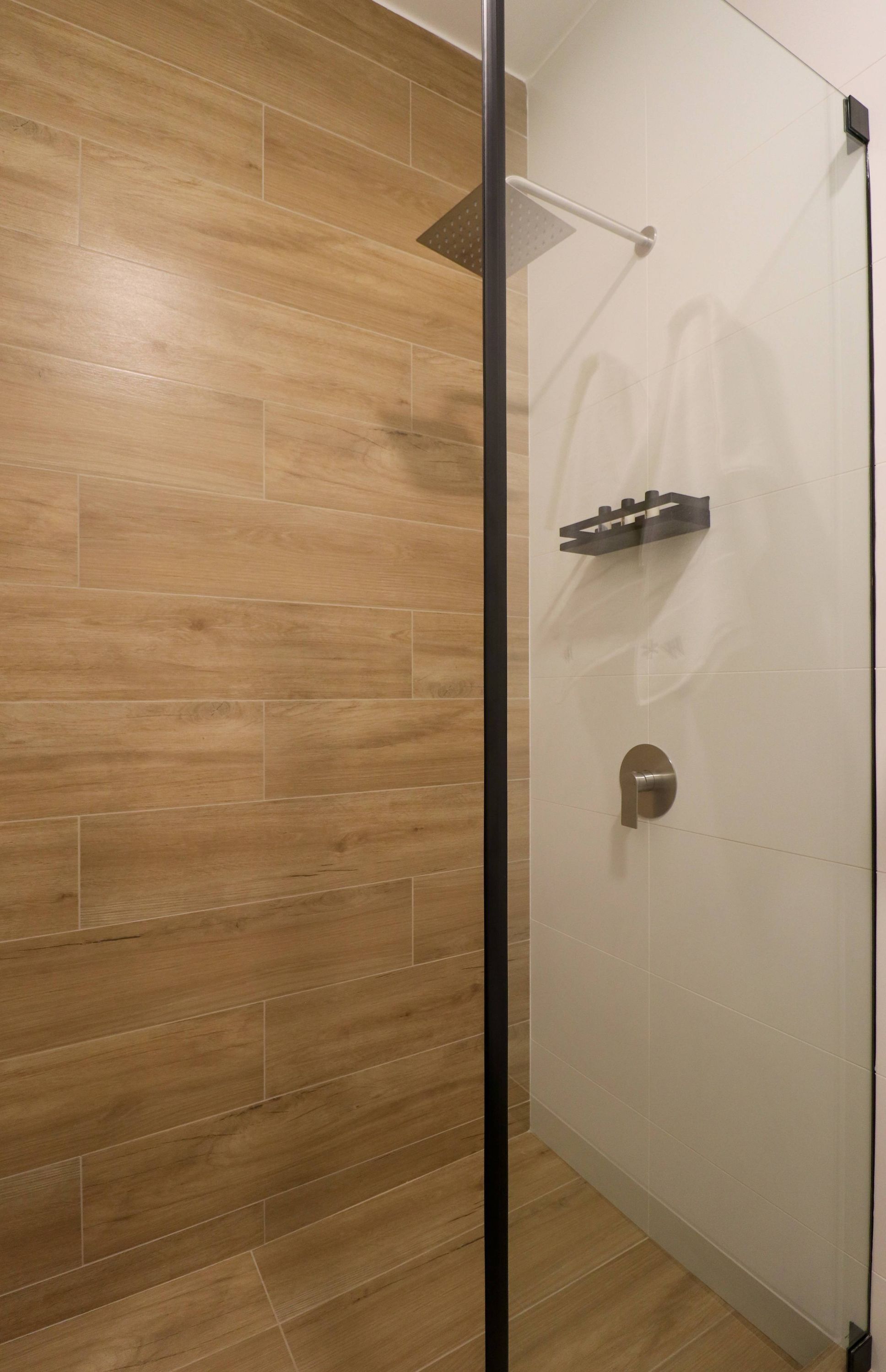 A shower with a glass door, a wooden floor, and a wall-mounted towel rack.