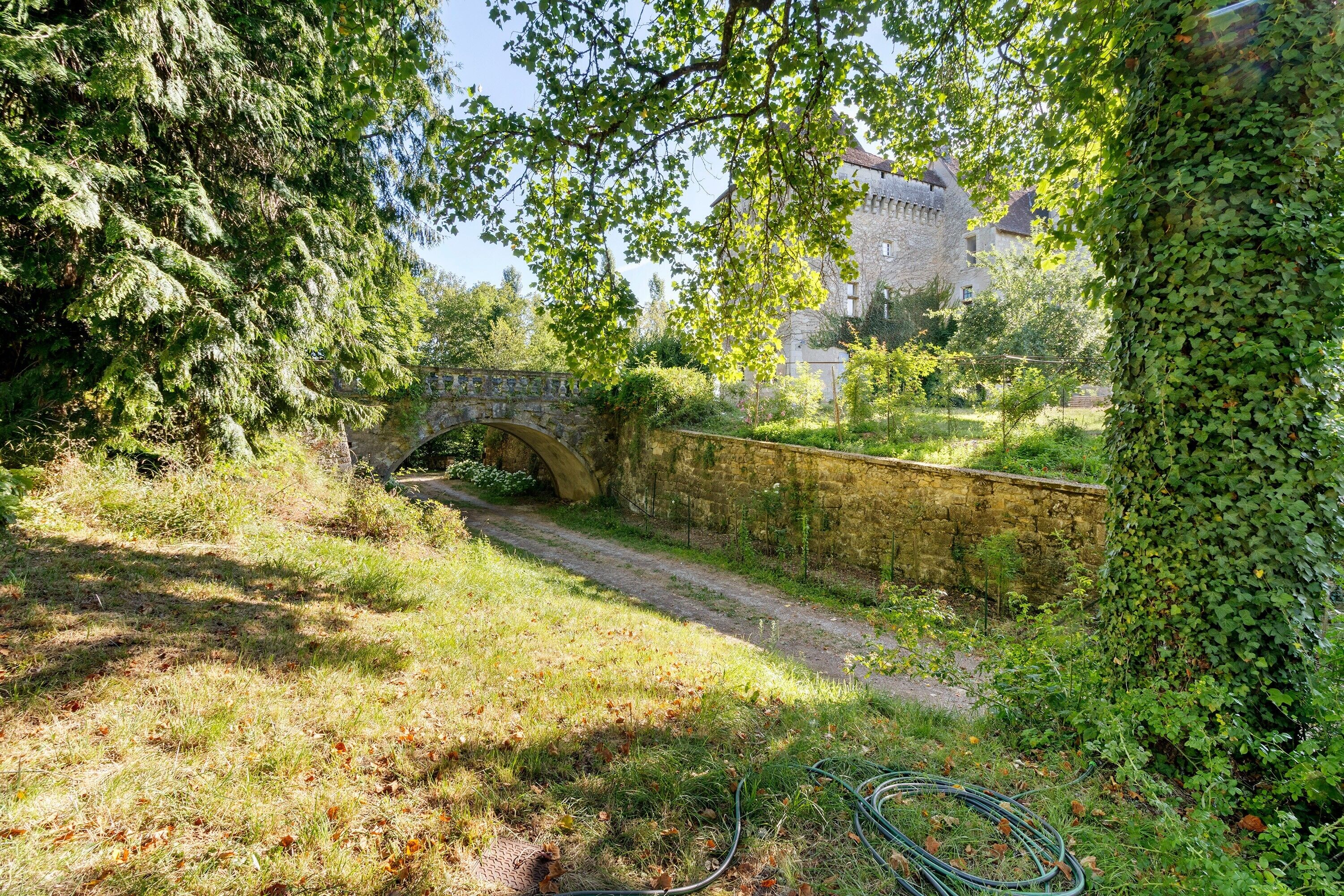A stone bridge over a narrow waterway, surrounded by lush greenery and a stone wall.