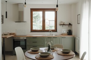 A modern kitchen with a dining area, featuring a large window, wooden cabinets, and a central island. - Aetna Apartment - Cratere Centrale (Nicolosi)