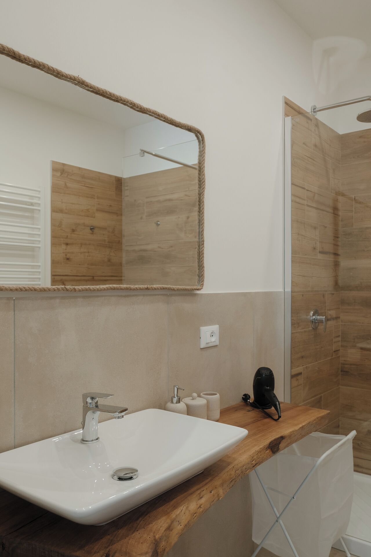 Une salle de bain avec un meuble-lavabo en bois, un grand miroir, un lavabo blanc et un espace douche.