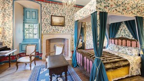 A room with a four-poster bed, a fireplace, a chair, and a table.