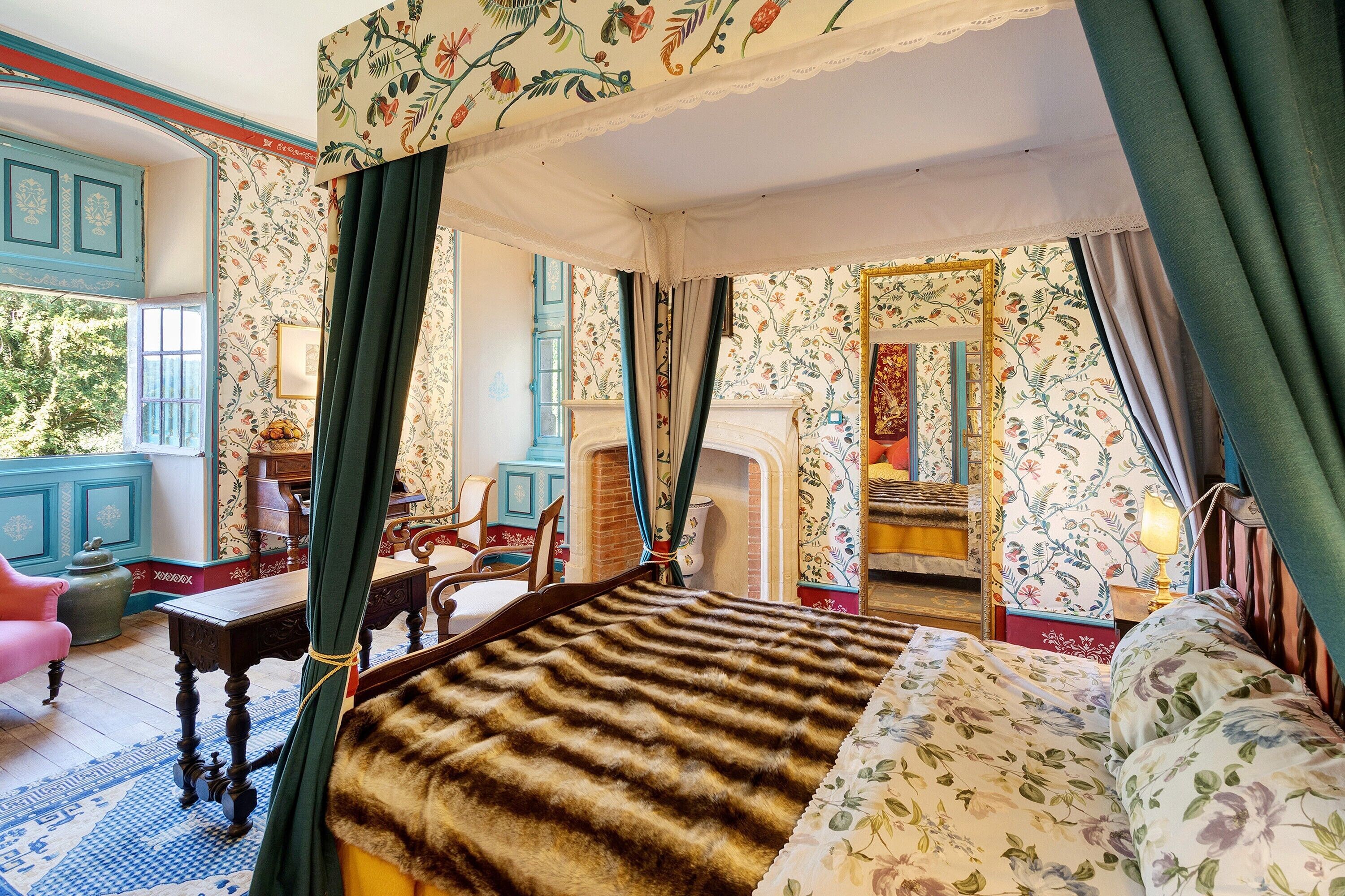 Een bed met hemel, een zithoek met stoel en tafel, en uitzicht op het landschap door een raam.
