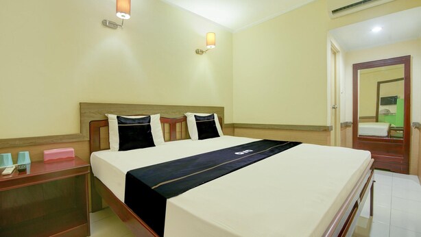 A hotel room with a bed, bedside tables, a nightstand, a wall-mounted lamp, and an air conditioning unit. - Family Luxury Suite W/free Wifi and Parking (Makassar)