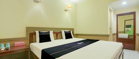 Une chambre d’hôtel comprenant un lit, des tables de chevet, une petite table, une lampe fixée au mur et un appareil de climatisation.