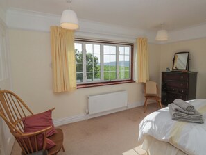 Ein Schlafzimmer mit Bett, Sessel, Kommode, Heizkörper und einem fenster mit Vorhängen.