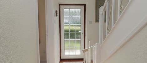 A hallway leading to a door with a frosted glass window, a white door frame, and a small rug on the floor.