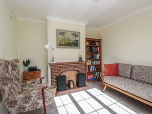Ein Wohnzimmer mit Kamin, Bücherregal, einem blumigen Sessel und einer Couch.