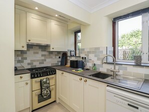 A modern kitchen with a gas stove, oven, and dishwasher, a window with a view of greenery, and a tiled backsplash. - Throstlegarth (Milnthorpe)