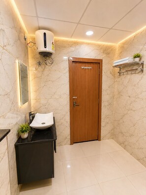 A bathroom with a marble wall, a wooden door, a sink with a mirror, and a towel rack. - Hotel Grand Dev Krishna (Ujjain)