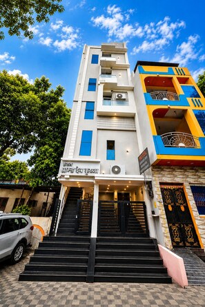 A hotel with a staircase leading to the entrance, a signboard with text, and a multi-story building with balconies. - Hotel Grand Dev Krishna (Ujjain)