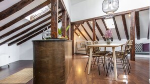 Une pièce de style loft avec des poutres en bois apparentes, une grande table à manger centrale entourée de chaises, une grande barrique en bois et un luminaire suspendu.