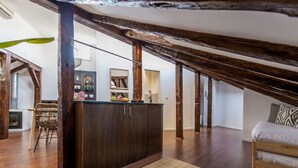 Une chambre à coucher de style loft avec des poutres en bois apparentes, une armoire en bois foncé, un tapis tissé et un lit agrémenté d’oreillers à motifs.