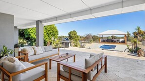 A covered outdoor seating area with a pool, barbecue, and a view of the surrounding landscape.