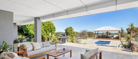 A covered outdoor seating area with a pool, barbecue, and a view of the surrounding landscape.