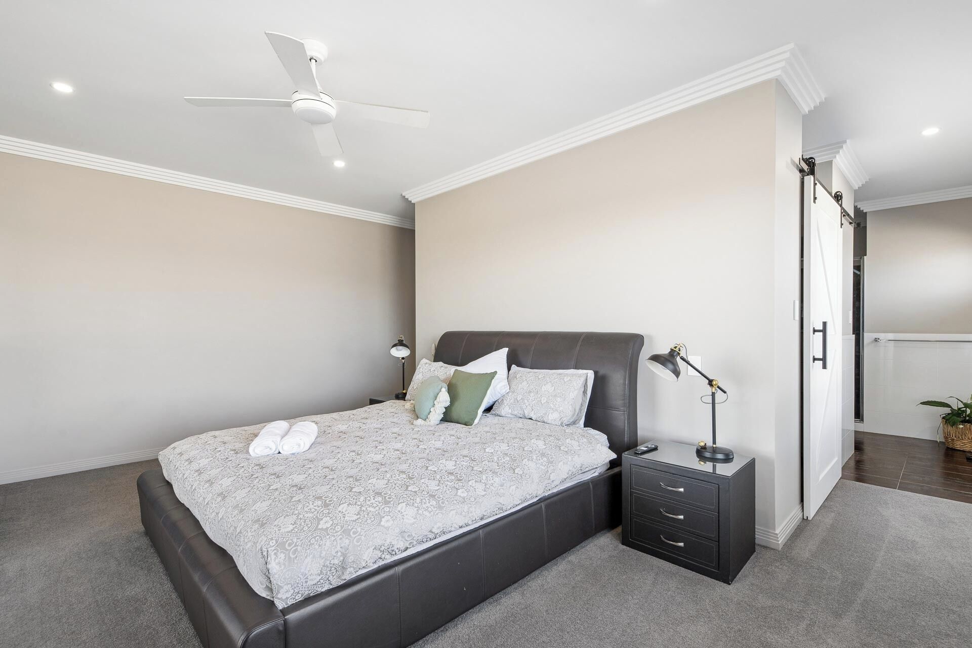 Una camera da letto con un letto, comodini, una ventola a soffitto e una porta che dà su un'altra stanza.