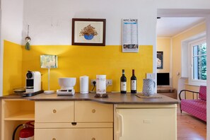 A kitchen with a yellow accent wall, a framed artwork, a calendar, and various kitchen appliances. - Apartment 'Casa Avisio' with Private Garden, Wi-Fi and Ski Slopes Nearby (Castello-Molina di Fiemme)
