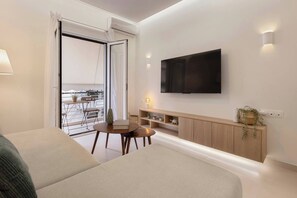 Een moderne kamer met een bank, een klein tafeltje, een aan de muur bevestigde televisie, een balkon met uitzicht en een houten kast met planken.