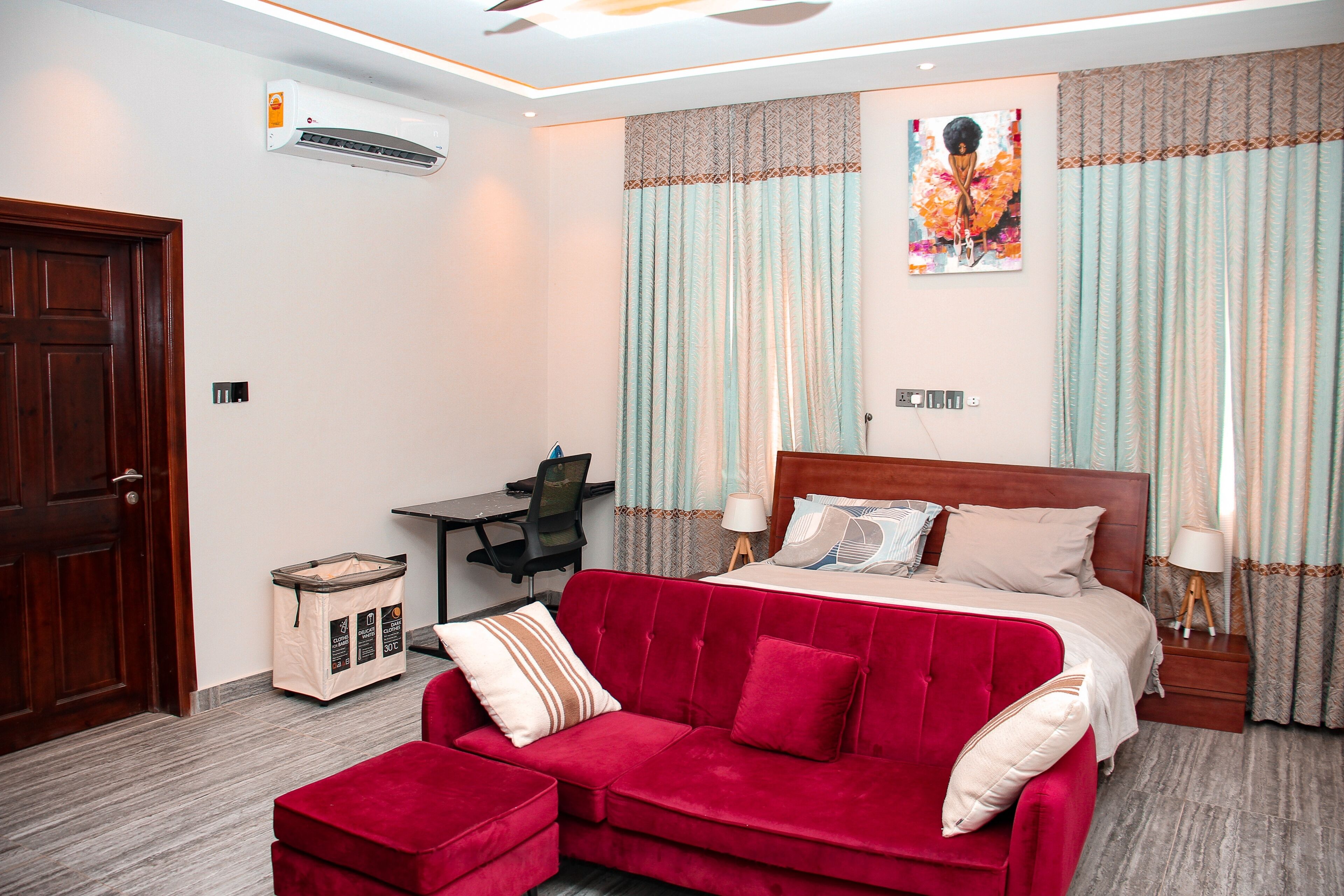 A hotel room with a bed, a red sofa, a desk, and a trash bin.