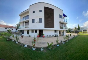 A modern multi-story building with a curved facade, balconies, and a landscaped garden. - Massive Dynamics by Oobake World Ltd.  (Adringanor, East legon)