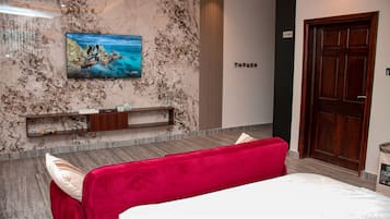 Habitación de hotel con una cama, un televisor montado en la pared, una puerta de madera y una pared con textura de mármol.