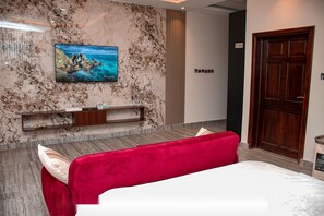 A hotel room with a bed, a TV mounted on the wall, a wooden door, and a marble-textured wall. - Massive Dynamics by Oobake World Ltd.  (Adringanor, East legon)