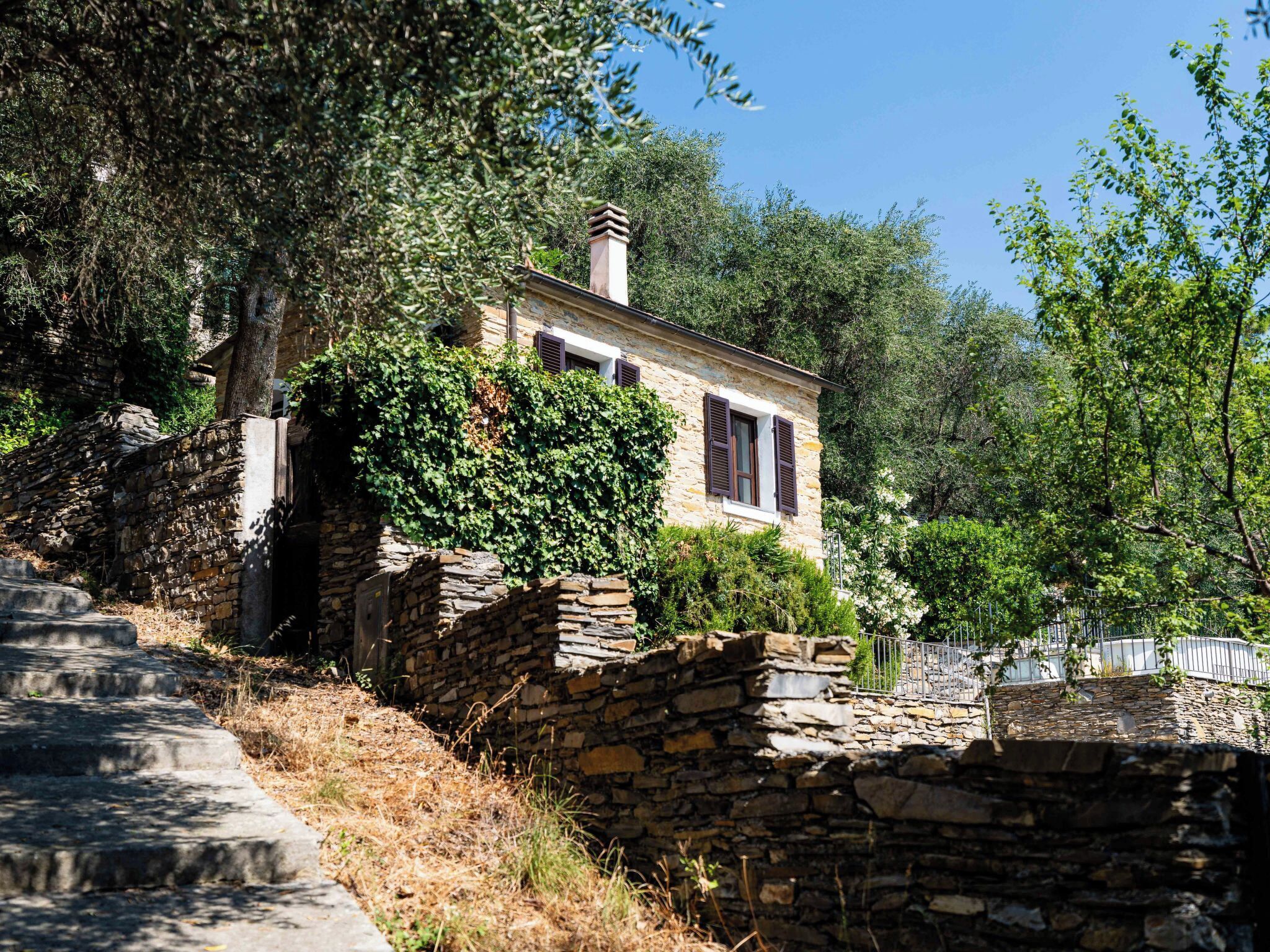 Una casa de piedra con una escalera de piedra que sube hacia ella, rodeada de vegetación.