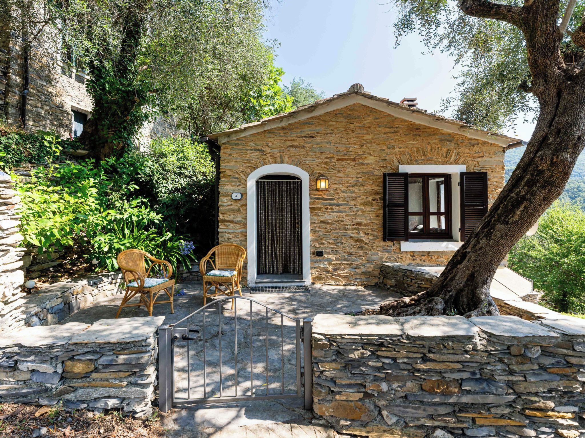 A stone house with a small porch, two wicker chairs, and a gate.