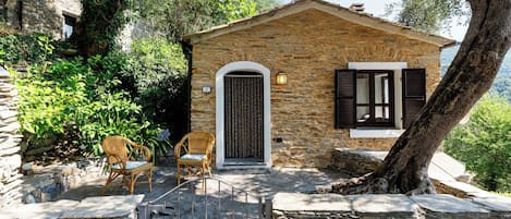 A stone house with a small porch, two wicker chairs, and a gate.