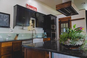 A kitchen with dark cabinets, a microwave, a sink, and a Coca-Cola sign. - HISTORIC 1945 SCHOOLHOUSE. 4700 sq. ft. of luxury five minutes from Lake Fork. (Como)