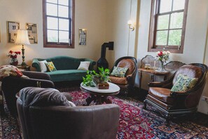 Une pièce au décor traditionnel, avec un canapé vert, des fauteuils en cuir, un tapis à motifs et une cheminée.