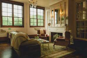 A spacious living room with a fireplace, large windows, and classic furniture. - HISTORIC 1945 SCHOOLHOUSE. 4700 sq. ft. of luxury five minutes from Lake Fork. (Como)