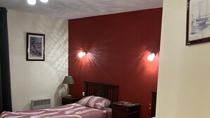Una habitación con dos camas, una silla, una mesita de noche, una lámpara y un aplique en el techo.