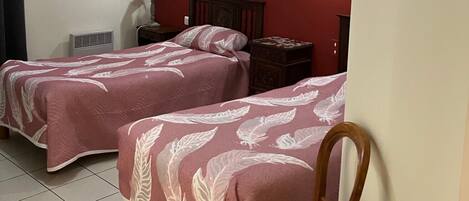 Ein Zimmer mit zwei Betten, einem Sessel, einem Nachttisch, einer Lampe und einer Deckenleuchte.