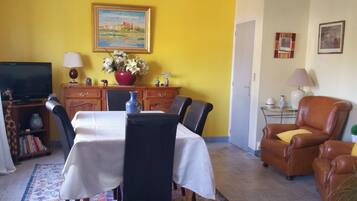 Zona pranzo con tavolo apparecchiato per quattro persone, televisione e libreria.