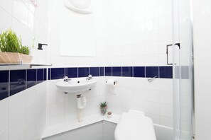 Ett modernt badrum med en vit tvättställ, en toalett, en dusch och en liten krukväxt.