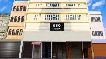A hotel with a sign reading 'HOTEL' and a company-serviced symbol. It has multiple floors with windows and a flat facade.