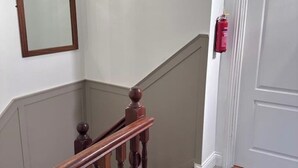 Una scala con balaustre in legno, una porta bianca e un estintore fissato al muro.