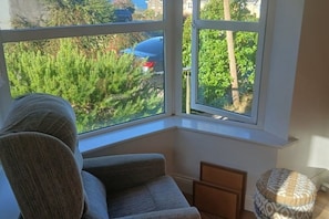 A corner room with a large window, a grey sofa, and a patterned ottoman.