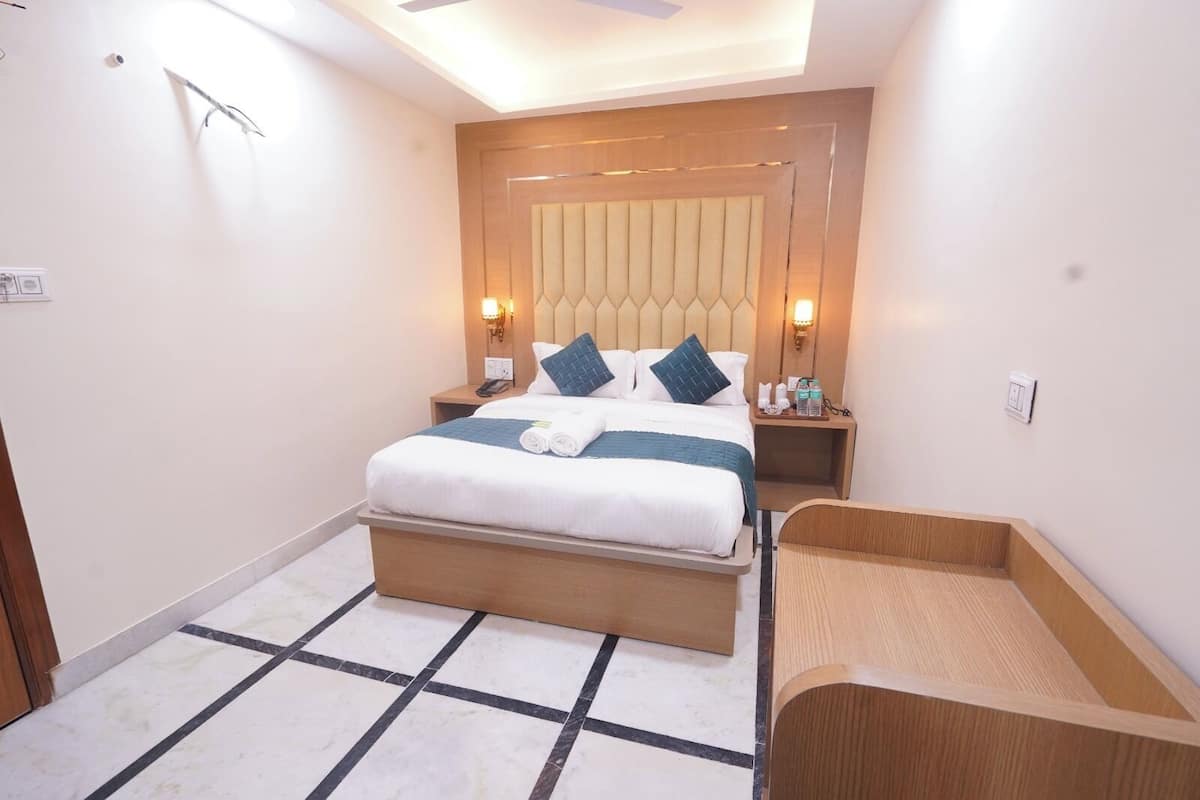 A hotel room with a bed, bedside tables, a wooden headboard, a small wooden bench, and a tiled floor.