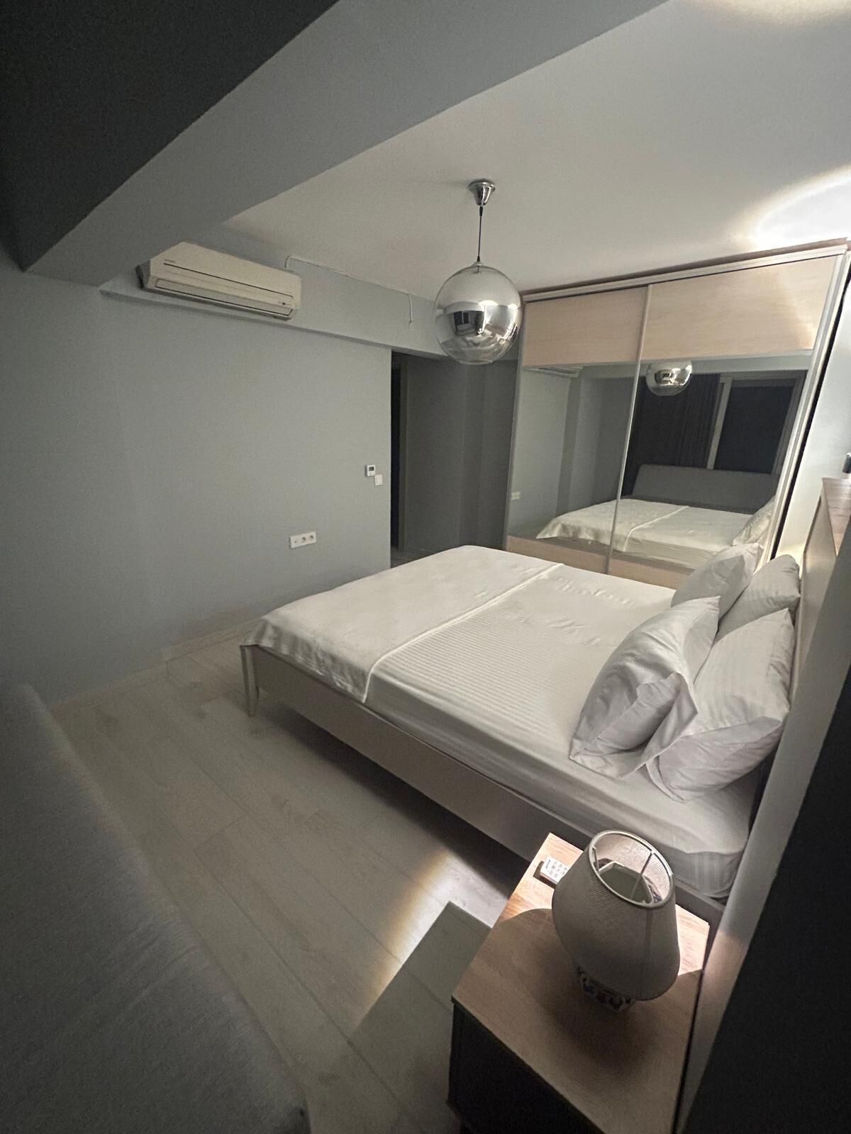 Um quarto moderno com cama, mesa de cabeceira, espelho e luminária no teto.